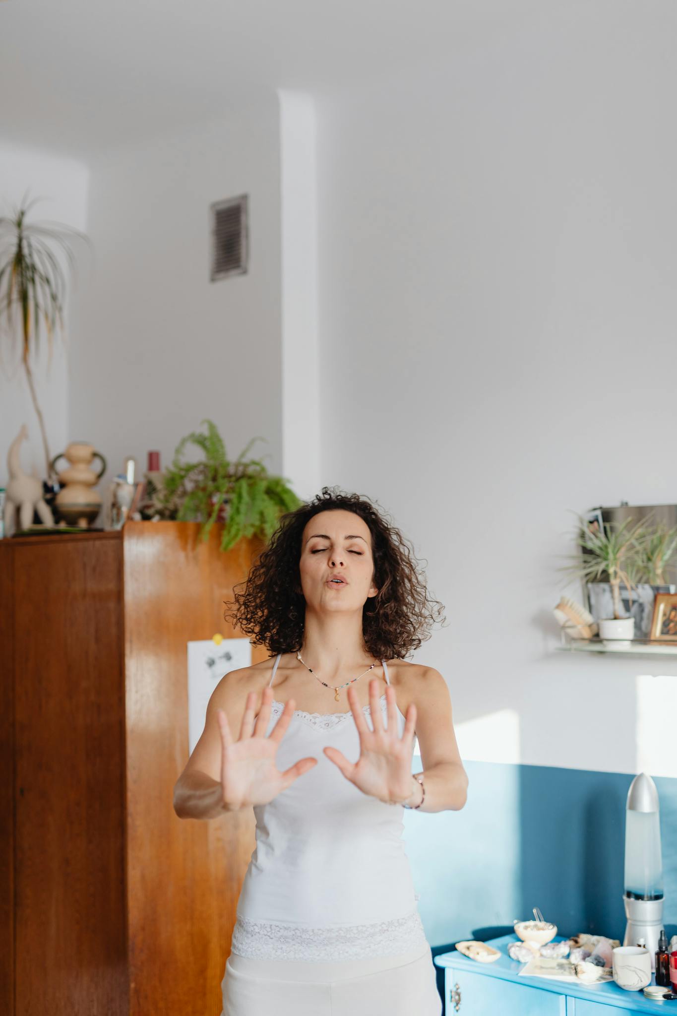 A young woman meditating with hands raised in a calm indoor setting.
